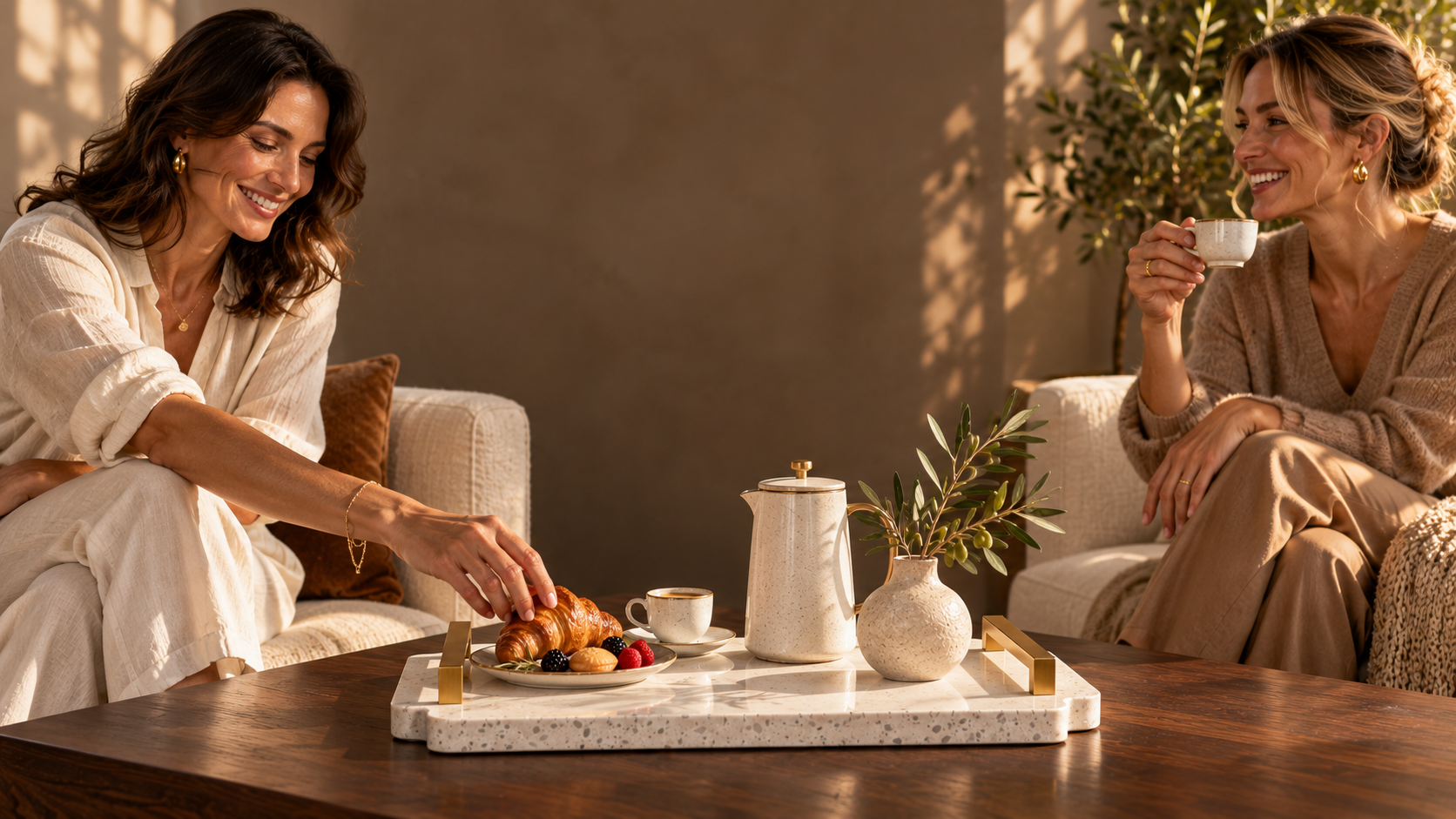 Two women enjoying coffee, one reaching for a pastry on the stone tray between them